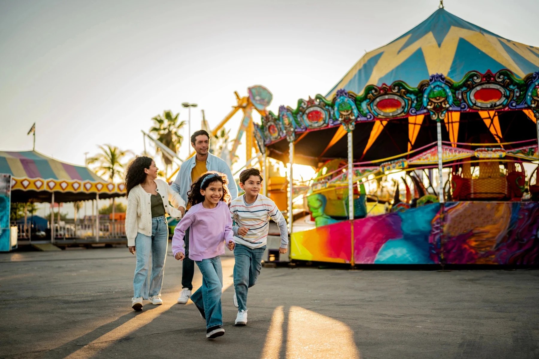 Siblings running through an amusement park at sunset